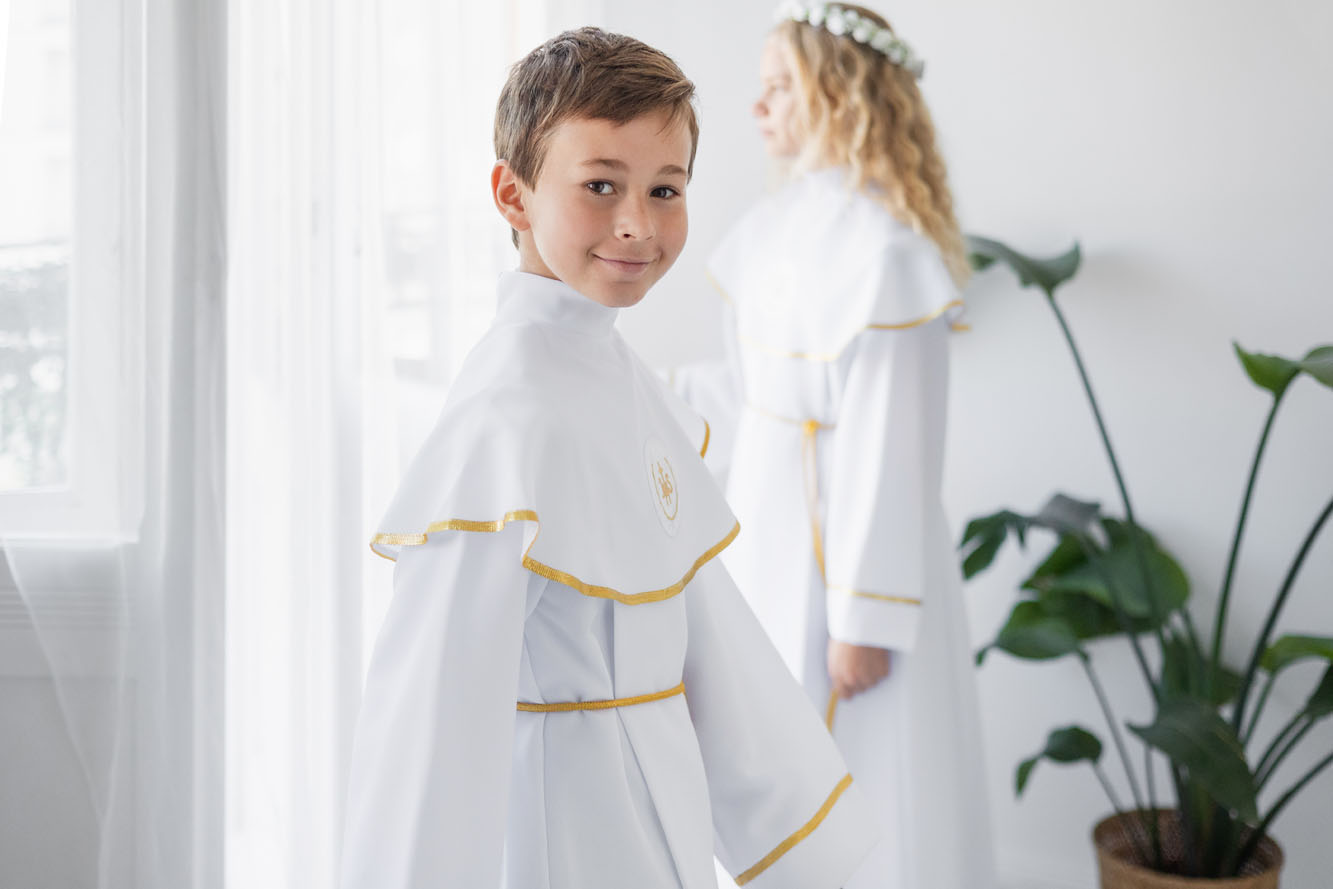 Chłopiec w albie komunijnej z pelerynką i złotymi zdobieniami